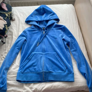 Blå hoodie från Juicy Couture - Säljer en snygg blå hoodie från Juicy Couture i mjukt material. Den har en dragkedja framtill och en broderad logga på bröstet. Den är i superbra skick, finns inga defekter! Det är bara att komma med prisförslag