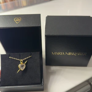 Halsband med hjärthänge från Maria Nilsdotter - Intressekoll på mitt superfina halsband från Maria Nilsdotter med ett hjärtformat hänge i guld och en klar sten i mitten. Hänget har en pil som går igenom hjärtat, vilket ger en unik och stilfull design. Perfekt för att ge en touch av lyx till din look.❣️✨🫶🏼Nypris 4495kr 