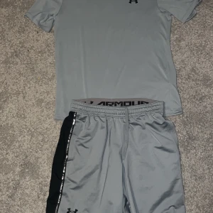 Grå t-shirt från Under Armour - Säljer en grå t-shirt från Under Armour med korta ärmar och logotyp på bröstet. Perfekt för träning med sitt lätta och bekväma material.