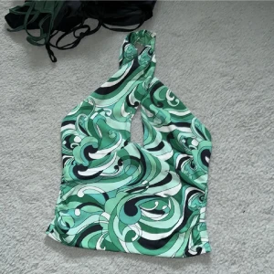 Grön mönstrad halterneck topp - Snygg grön halterneck topp med ett mönster i olika nyanser. Toppen har en unik design med knytning i nacken och en liten öppning framtill. Perfekt för en somrig look!