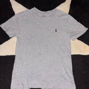 Grå t-shirt från Polo Ralph Lauren - Snygg grå t-shirt från Polo Ralph Lauren med korta ärmar och en liten broderad logga i blått på bröstet. Perfekt för en avslappnad stil.