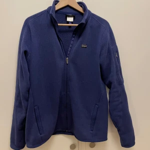  Patagonia flecce - Säljer en blå fleecejacka från Patagonia med dragkedja och hög krage. Jackan har långa ärmar och en liten Patagonia-logga på bröstet. Perfekt för kyliga dagar.