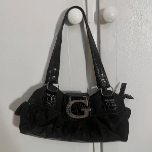 Vintage väska - Snygg svart axelväska med ett spänne framtill. Väskan har glansiga detaljer och ett krokodilmönstrat handtag. Ca 34cm i mått tvärsöver så en medelstor handväska med två separata fack på insidan!