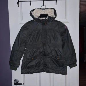 Mörkgrå parkajacka från Lindex - Säljer en mörkgrå parkajacka från Lindex. Jackan har dragkedja och knappar framtill samt praktiska fickor. Perfekt för kyliga dagar!