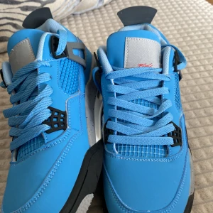 Blå Nike Air Jordans - Snygga blå Nike Air Jordans med svarta och grå detaljer. Skorna har en klassisk snörning och en unik design med stänkdetaljer på hälen. Perfekta för den som vill ha en stilren och sportig look.