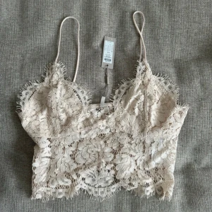 Beige spetslinne - Snyggt beige spetslinne med tunna axelband och vacker blommig spetsdesign. Perfekt för en somrig look eller att bära under en kavaj. Linnet är croppat. Storlek M men passar en S 