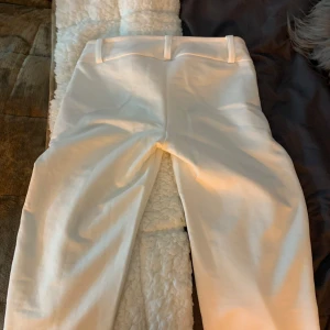 Kostym byxor low wayst  - Snygga vita byxor med låg midja. De har en stilren design med knappar framtill och bälteshällor. Perfekta för en elegant look.