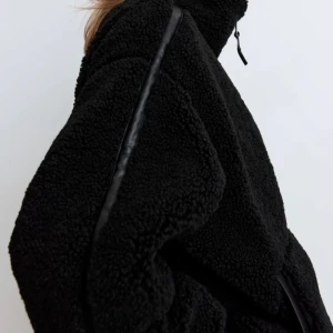 Ny Svart teddyjacka storlek XS från H&M - Ny och oanvänd pilejacka. Mysig svart teddyjacka med dragkedja framtill och hög krage. Jackan har två stora fickor och en loose passform, perfekt för kyliga dagar. Storlek XS som oversized. 