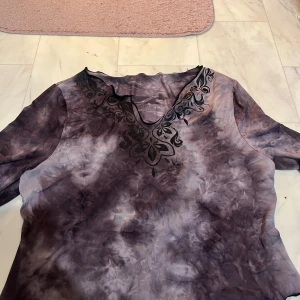 Lila blus med broderad v-ringning - Säljer en lila blus med ett vackert broderi vid v-ringningen. Blusen har långa ärmar och ett unikt mönster i olika lila nyanser. Perfekt för en bohemisk stil.