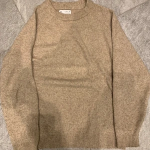 Beige stickad tröja  - Säljer en stilren beige stickad tröja. Perfekt för kyligare dagar med sin mjuka och bekväma passform. Tröjan har långa ärmar och ribbstickade muddar vid ärmslut och nederkant.