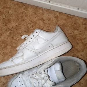 Vita Nike Air Force sneakers - Säljer ett par klassiska vita Nike Air Force sneakers. De har en stilren design med snörning och en robust sula. Perfekta för en casual look. Äkta