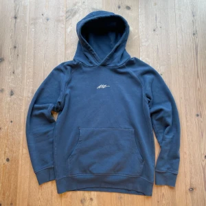 Blå hoodie från Next - Säljer en snygg blå hoodie från Next med en liten vit logga på bröstet. Den har en klassisk känguruficka och långa ärmar. Står att det är storlek 82 vilket motsvarar S. Hör av dig vid intresse!