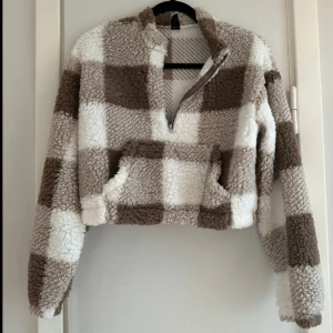 Rutig teddyjacka från Shein - Mysig teddytröja från Shein i brunt och vitt rutmönster. Jackan har en halv dragkedja framtill och en stor ficka på magen. Perfekt för kyliga dagar när du vill vara både varm och stilren.  Storlek: S Sparsamt använd   Mått  Byst: 46 cm Längd: 45 cm  Axelbredd: 47 cm Insida arm: 48 cm