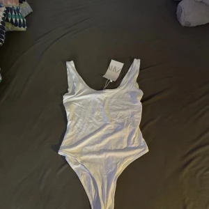 Vit bodysuit från Zara - Säljer en stilren vit bodysuit från Zara. Den är ärmlös och har en enkel design som passar perfekt till olika outfits. Perfekt för en minimalistisk look.