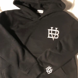 Svart hoodie från Bvaldi  - Säljer en svart hoodie från Bvaldi  med vit logga på bröstet och ärmen. Tröjan har en klassisk design med huva och långa ärmar. Perfekt för en avslappnad stil.
