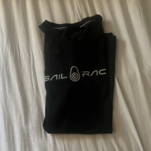 Svart t-shirt från Sail Racing - Snygg svart t-shirt från Sail Racing med tryck på framsidan. Perfekt för en avslappnad stil. Den har korta ärmar och en klassisk passform. Enkelt och stilrent plagg för alla tillfällen.