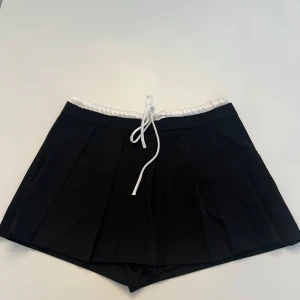 Svarta shorts från Zara - Snygga svarta shorts från Zara med vit resårmidja och knytband. Perfekta för en stilren look. Tillverkade i ett mjukt material som ger en bekväm passform.