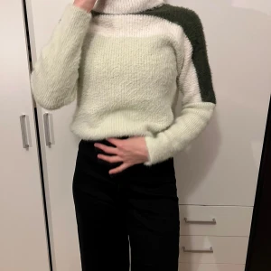 Stickad polotröja i grönt och vitt - Mysig stickad polotröja i grönt och vitt. Perfekt för kyliga dagar med sin varma och sköna känsla. Tröjan har en hög krage och långa ärmar, vilket gör den idealisk för höst och vinter. Den har en unik färgblockdesign som ger en modern touch.