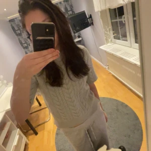 Grå stickad tröja från Amisu - Säljer en mysig grå stickad tröja från Amisu. Tröjan har ett klassiskt flätmönster och korta ärmar, perfekt för lager-på-lager under kyliga dagar. Den är i storlek 34 och passar utmärkt för både vardag och avslappnade tillfällen.