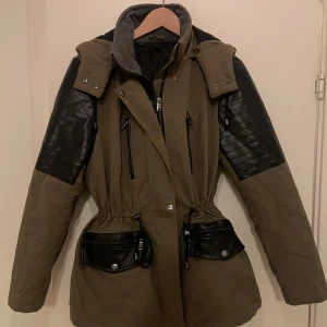 Parkas - Rainbow  - .Parkas med avtagbar huva, dragkedja och knappar framtill. Två större flickor med snyggt lock med dragkedja som design. Även två mindre fickor vid bröstet. Svart läderdetaljer på ärmarna och fickorna. Snörning i midjan.  Bekväm och varm vinterjacka. Storlek: 42  Endast använd en månad. Inga skador eller fläckar. Nyskick.  Nypris: 1000:-