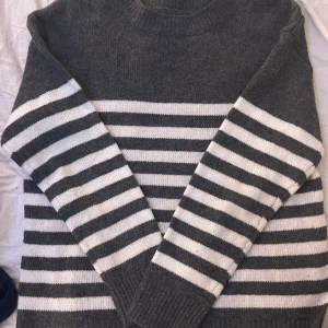 Grå och vit randig stickad tröja - Säljer en mysig grå och vit randig stickad tröja med långa ärmar. Perfekt för kyliga dagar och ger en stilren look. Tröjan har en klassisk rund halsringning och ribbade muddar. Tröjan e från shein