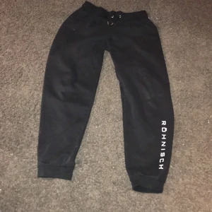 Svarta mjukisbyxor från Röhnisch - Säljer ett par svarta mjukisbyxor från Röhnisch med elastisk midja och snörning. Byxorna har en avslappnad passform och är perfekta för en bekväm dag hemma. Röhnisch-loggan finns tryckt på benet.