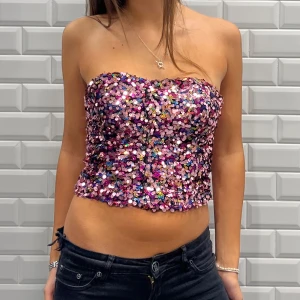 Rosa paljett tubtopp - Snygg och glittrig tubtopp täckt av färgglada paljetter. Perfekt för en festlig kväll. Toppen är axelbandslös och croppad, vilket ger en trendig look.