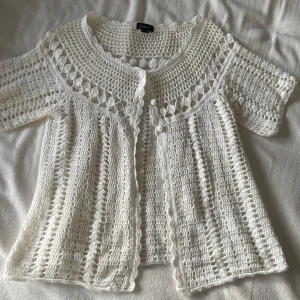 Vit virkad kofta från Lindex - Säljer en superfin vit virkad kofta från Lindex. Den har korta ärmar och en söt knäppning framtill. Perfekt för vår och sommar, och ger en romantisk touch till vilken outfit som helst. Passar både till vardags och festliga tillfällen. (Aldrig använd) 🌸