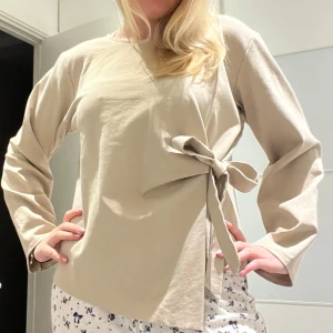Beige långärmad topp med knyte - Beige topp med långa ärmar och en snygg knytning i sidan. En asymmetrisk design och knytet går att knyta upp o göra om som man vill. Köpt i Grekland och passar storlek S🩷🩷 aldrig använd