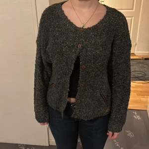 Grå kofta med knappar - Mysig grå kofta med knappar framtill. Den har en normal passform och långa ärmar, perfekt för kyligare dagar. Koftan har en texturerad yta som ger en extra dimension till din outfit.