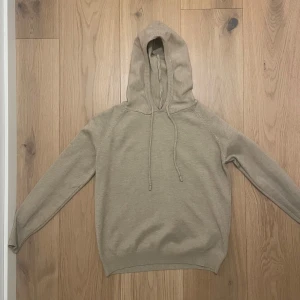Beige kaschmir hoodie - Säljer en stilren beige hoodie med dragsko i huvan. Perfekt för en avslappnad look. Tröjan har långa ärmar och ribbade muddar vid ärmslut och nederkant.