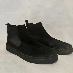 Svarta Chelsea boots från The Original Playboy - Snygga svarta Chelsea boots i mocka med elastiska paneler på sidorna för enkel på- och avtagning. De har en robust sula som ger bra grepp. Använda endast några få gånger, nyskick. 