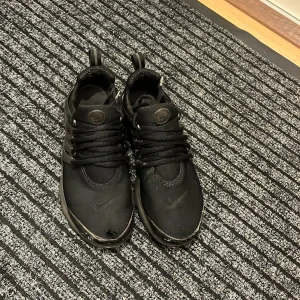 Svarta Nike prestos  - Säljer ett par svarta Nike prestos i bra skick men ena skon har ett litet hål i framsidan.De har en stilren design med snörning och är perfekta för vardagsbruk. 