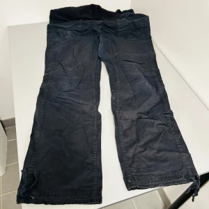 Svarta byxor från H&M Mama - Säljer ett par svarta byxor från H&M Mama i bra skick. Byxorna har en loose passform och är högmidjade med en bekväm stretchpanel för graviditet. De har praktiska fickor och knappar som detaljer. Perfekta för vardagsbruk under graviditeten.