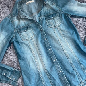 Blå jeansskjorta - Säljer en snygg blå jeansskjorta från Denim. Skjortan har långa ärmar och knappar framtill. 