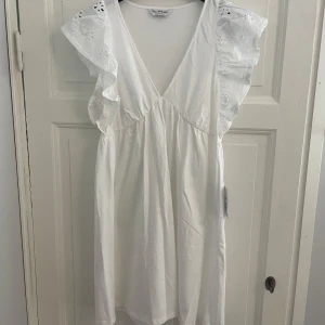 Vit klänning med volangdetaljer - Säljer en superfin vit klänning med volangdetaljer på axlarna. Den har en v-ringad design och är perfekt för sommardagar. Klänningen är idealisk för både vardag och fest. Passformen är normal och den är i nytt skick. ⭐️ Nypris 329kr. 