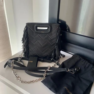 Svart axelväska med fransar från Maje - Snygg svart axelväska från Maje med fransar och nitar i ett zigzag-mönster. Fint skick i lilla modellen 🩷(kommer inte sälja endast kedjan)