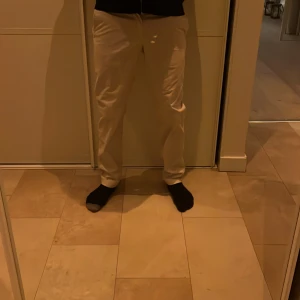 Beige chinos från J.Lindeberg - Snygga beige chinos från J.Lindeberg med en klassisk passform. Byxorna har knappar och är perfekta för en stilren look. Tillverkade i ett bekvämt material som passar bra till olika tillfällen.