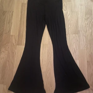 Svarta bootcut byxor från Ginatricot - Säljer ett par svarta byxor med en snygg och trendig bootcut-stil. De är perfekta för både vardag och fest. Byxorna har en hög midja som ger en smickrande passform. Materialet är mjukt och bekvämt, vilket gör dem sköna att bära hela dagen. Passar perfekt till en stickad tröja eller en snygg blus.