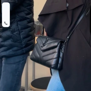 Svart quiltad axelväska Ysl  - Snygg svart quiltad axelväska med elegant design. Perfekt för att bära dina nödvändigheter med stil. Väskan har en justerbar rem och en dekorativ detalj på framsidan.