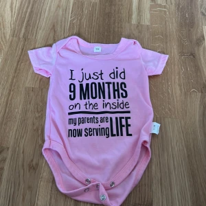 Rosa babybody med text - Söt rosa babybody med korta ärmar och rolig text på framsidan. Perfekt för de minsta med tryckknappar i grenen för enkel på- och avklädning.