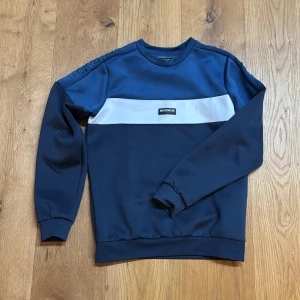 Blå tröja från McKenzie - Snygg blå tröja från McKenzie med en vit horisontell rand över bröstet och broderad logga på ärmen. Perfekt för en avslappnad stil. Storleken är 12-13 år men passar dig som är 165-170