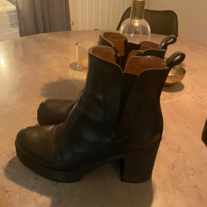 Svarta boots från Urban Project - Säljer ett par snygga svarta boots från Urban Project. De är i skinn och har en rejäl klack som ger lite extra höjd. Perfekta för höst och vinter, och funkar lika bra till vardags som till fest. De har en dragkedja på sidan för enkel på- och avtagning.