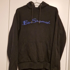 Svart hoodie från Ben Sherman - Säljer en svart hoodie från Ben Sherman i bra skick. Den har en stor Ben Sherman-logga i blått på framsidan och en klassisk känguruficka. Perfekt för höst och vinter, med en mysig huva och dragsko. Passar både till vardags och chillkvällar. 🖤