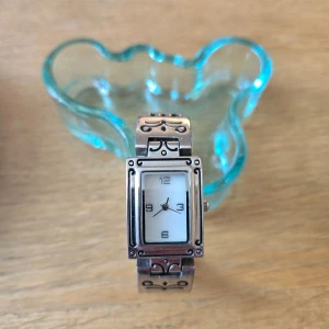 Elegant silverfärgad klocka med rektangulär urtavla - Säljer en stilren och elegant klocka i silverfärg med en rektangulär urtavla. Klockan har en vit urtavla med svarta siffror och visare. Armbandet är detaljerat med små dekorativa mönster. Perfekt för både vardag och fest!