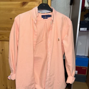 Ralph Lauren skjorta - Säljer en snygg rosa skjorta från Ralph Lauren i storlek S. Skjortan är i bomull och har en klassisk design med knappar och långärmade ärmar. Perfekt för både vardag och festliga tillfällen. Den är i mycket bra skick och redo för en ny ägare!