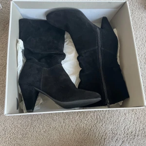 Svarta mockastövlar från Tamaris - Säljer ett par helt nya/oanvända svarta stövlar i mocka från Tamaris. De har en bekväm klack och dragkedja på sidan för enkel på- och avtagning. Perfekta för höst och vinter, både till vardags och fest. Använd dem för att ge din outfit en stilfull touch!💕(ny pris 900kr)