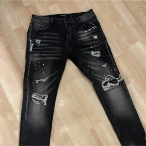 Svarta slitna jeans från Zavetti - Säljer ett par svarta jeans från Armani i bra skick. De har en cool, sliten look med hål och slitningar på benen. Perfekta för en avslappnad stil. Passar bra till både vardag och fest!