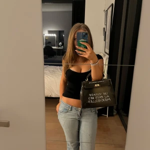 Svart handväska med text - Snygg svart handväska med vit text på framsidan. Väskan har en stilren design och en kedja som axelrem, vilket ger den en modern touch. Perfekt för både vardag och fest!