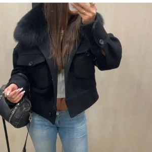 Meotine jacka - Säljer en snygg svart jacka med en lyxig pälsdetalj på kragen. Jackan har en klassisk design med knappar framtill och stora fickor. Perfekt för höst och vinter, och ger en elegant touch till vilken outfit som helst. Passar bra till både vardag och fest!
